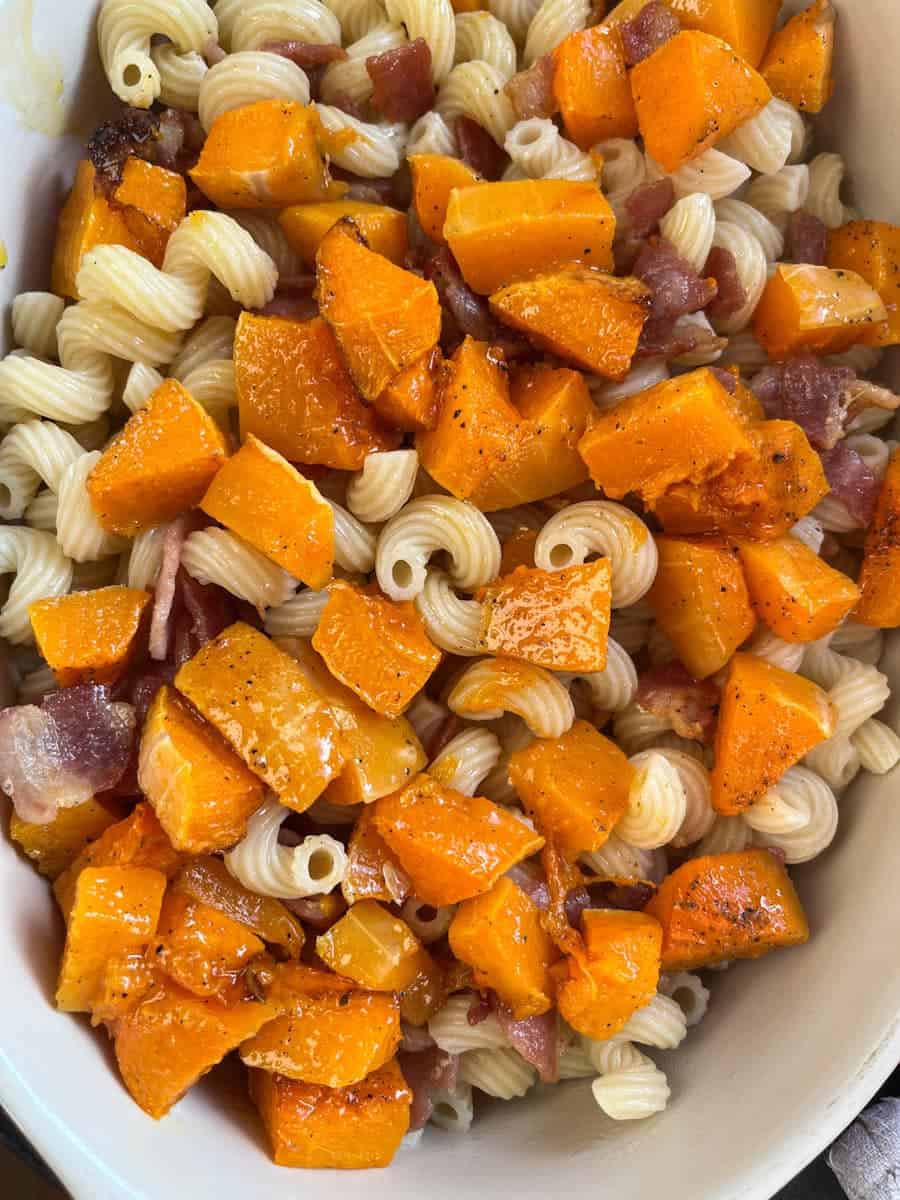 Macaroni in a baking dish with cooked bacon and roasted pumpkin cubes.