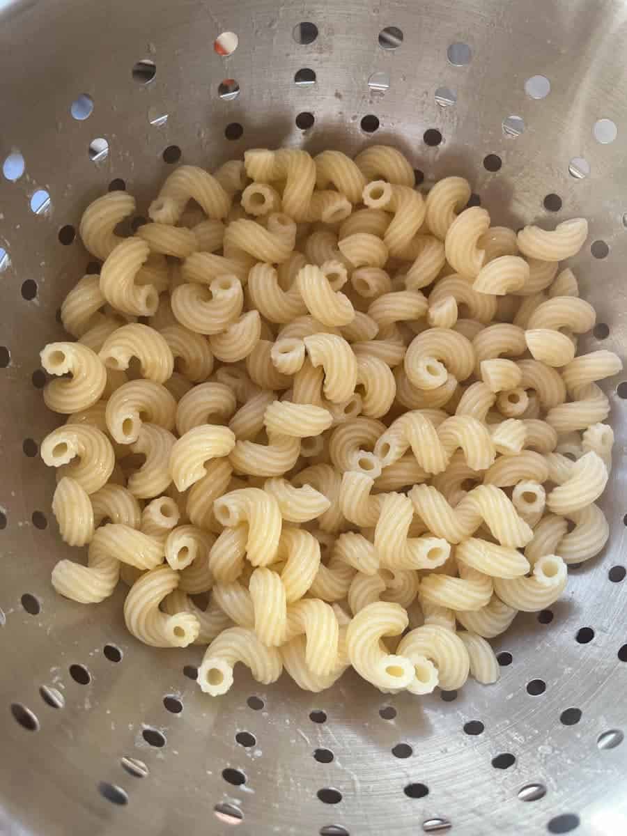 Cooked macaroni in a silver colander.