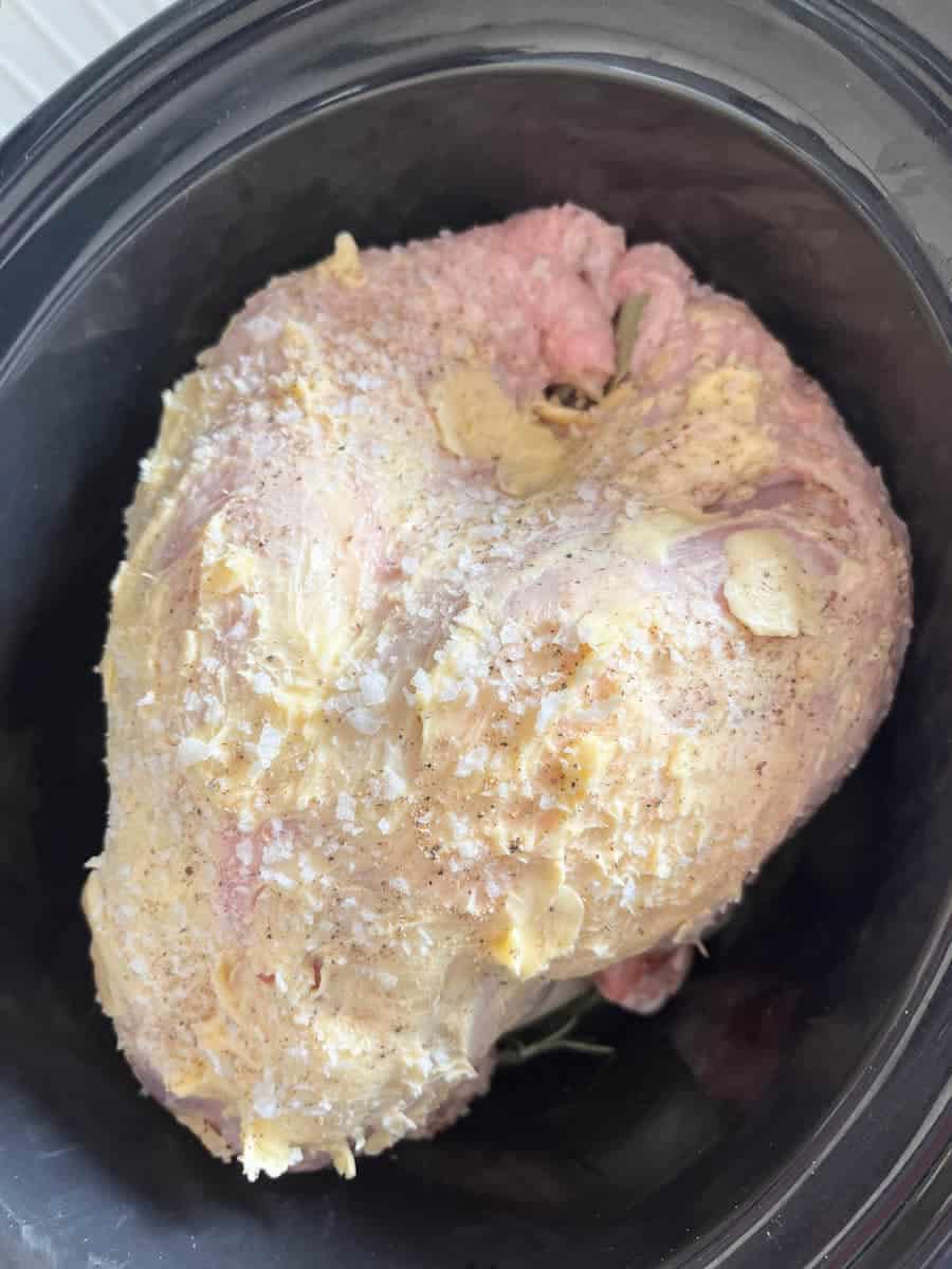 A turkey crown covered in butter and salt inside a slow cooker pot.