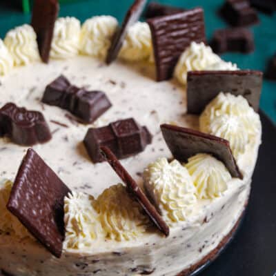 An after eight cheesecake decorated with whipped cream and after eight chocolates on a black plate.