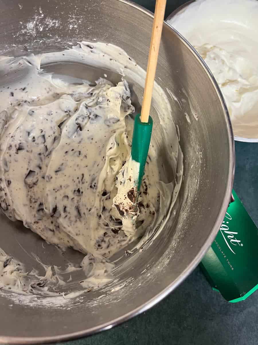 A silver bowl of cheesecake filling with grated chocolate, chopped after eights and a green spatula.