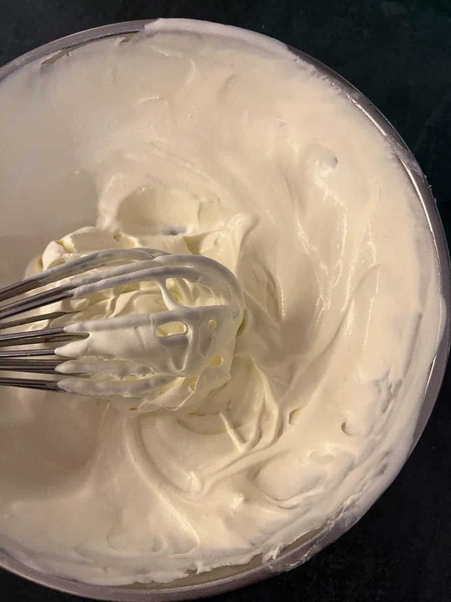 A silver bowl of whipped cream with a silver whisk.