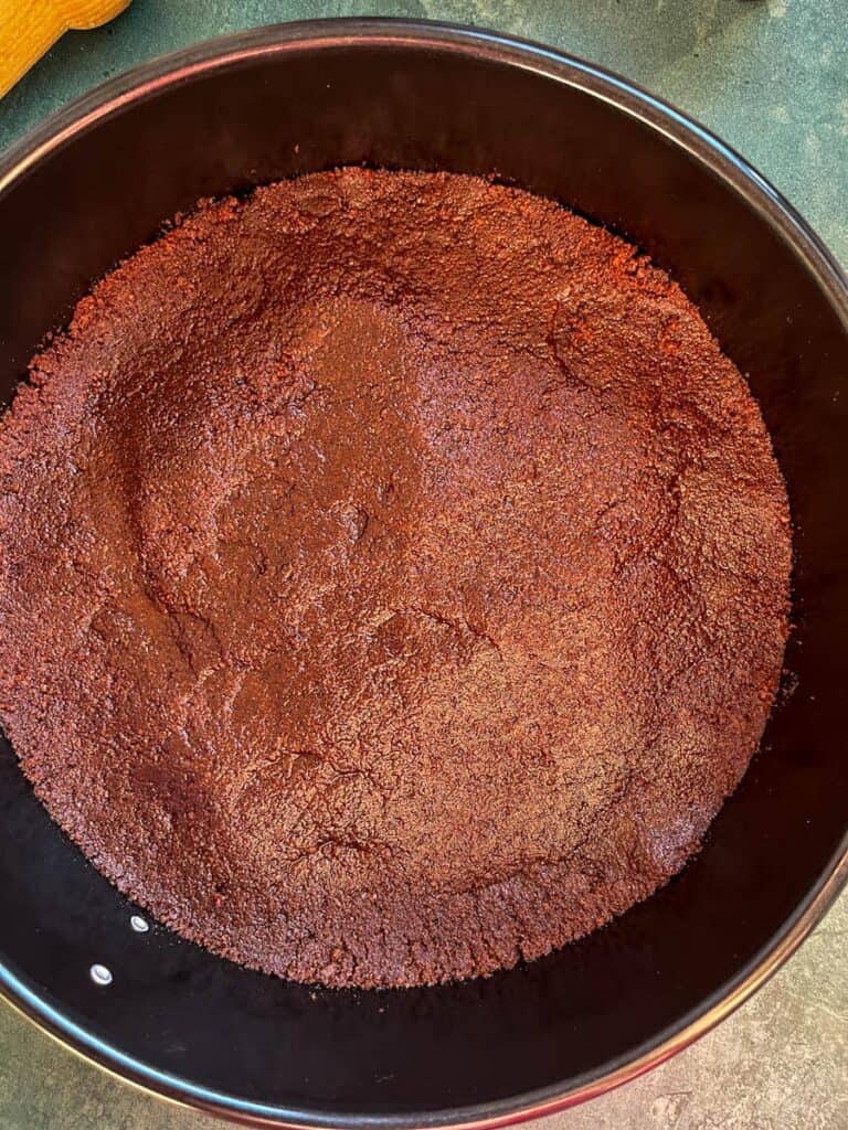 A chocolate biscuit base pressed into a round black springform cake tin.