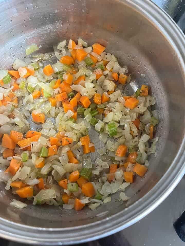 diced onions, celery and carrots cooking in olive oil in a silver saucepan.