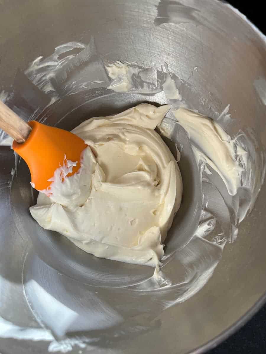 Whipped Cream cheese in a silver bowl and an orange spatula.