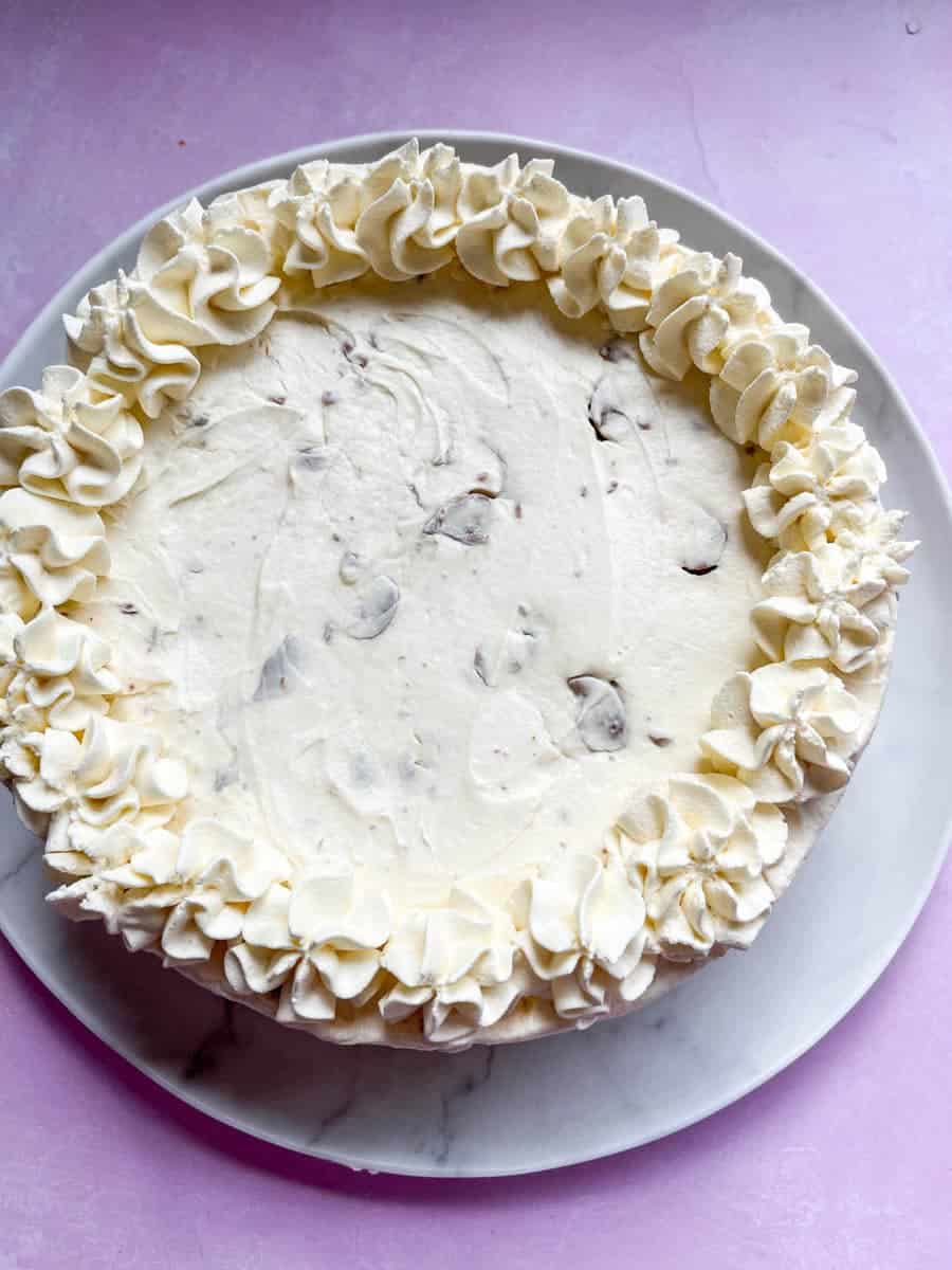 A no bake cheesecake decorated with whipped cream on a white plate and pink backdrop.
