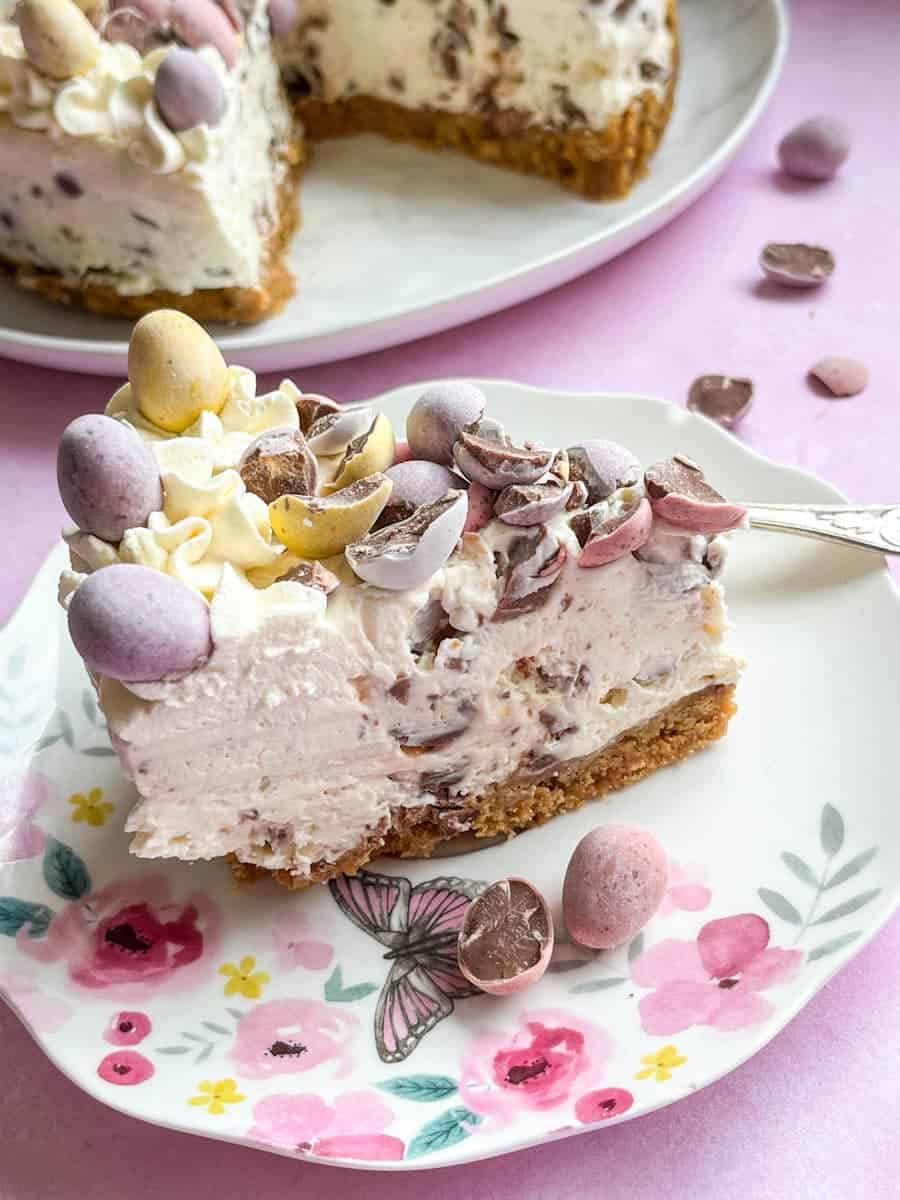 A slice of no bake cheesecake with mini chocolate Easter eggs on a pink and white floral plate.