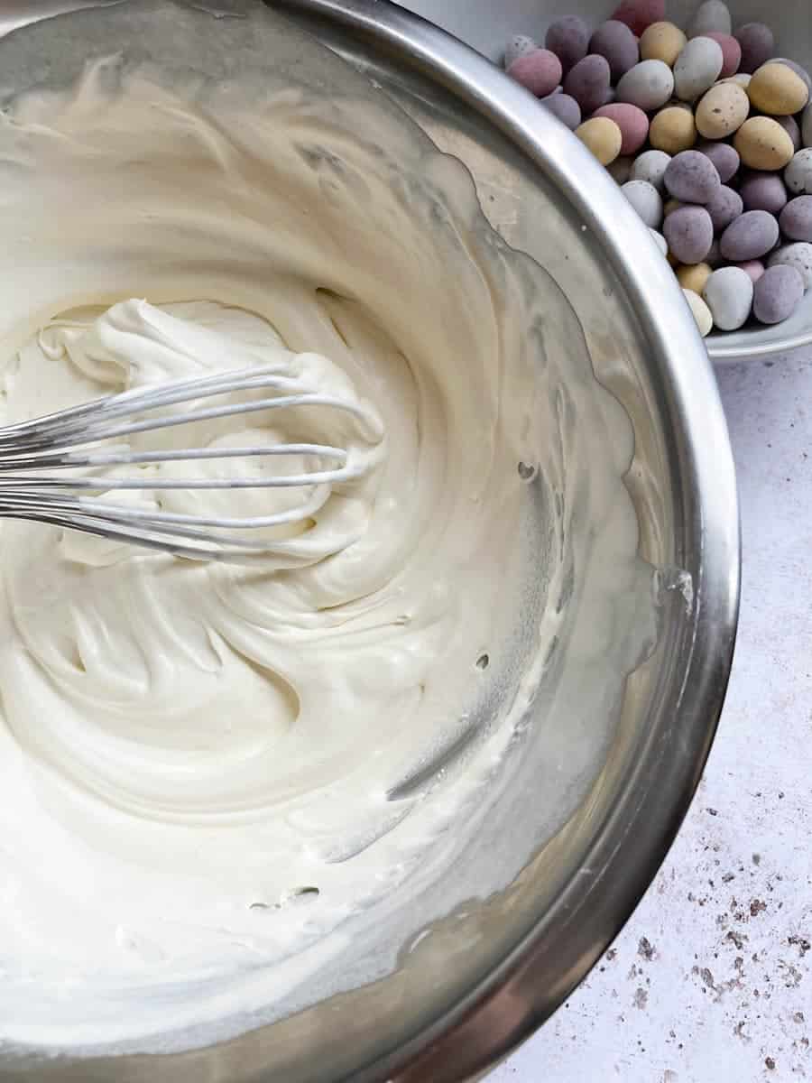 A large silver bowl of whipped cream with a silver whisk and a bowl of mini eggs.