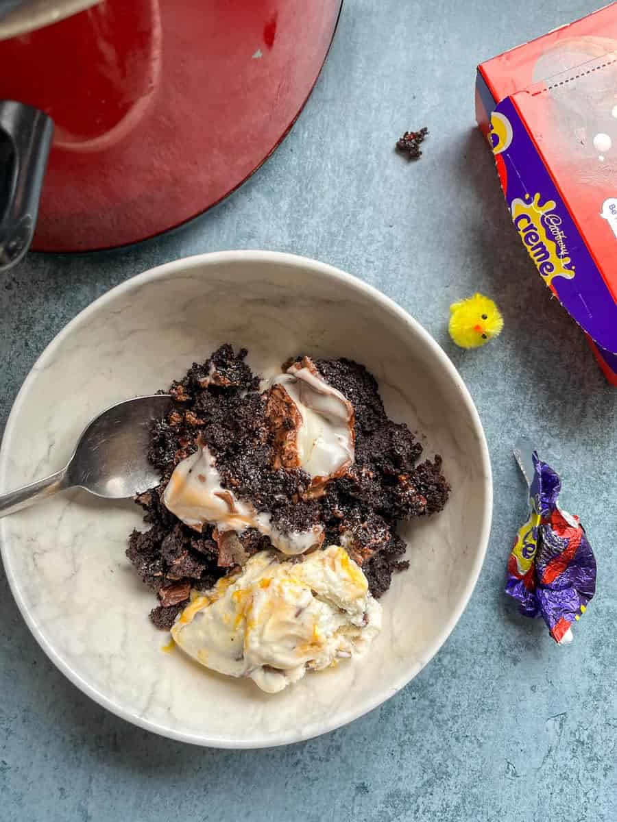 A white bowl of chocolate sponge cake with creme eggs and a scoop of ice cream.