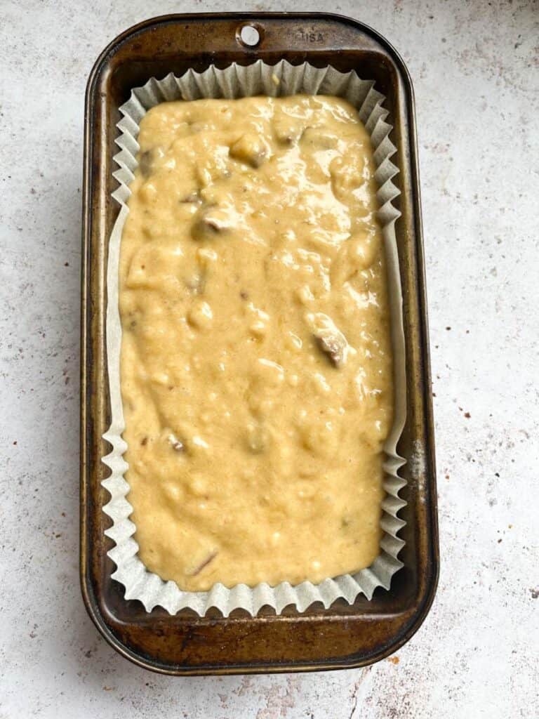 Banana bread batter poured into a lined loaf tin.