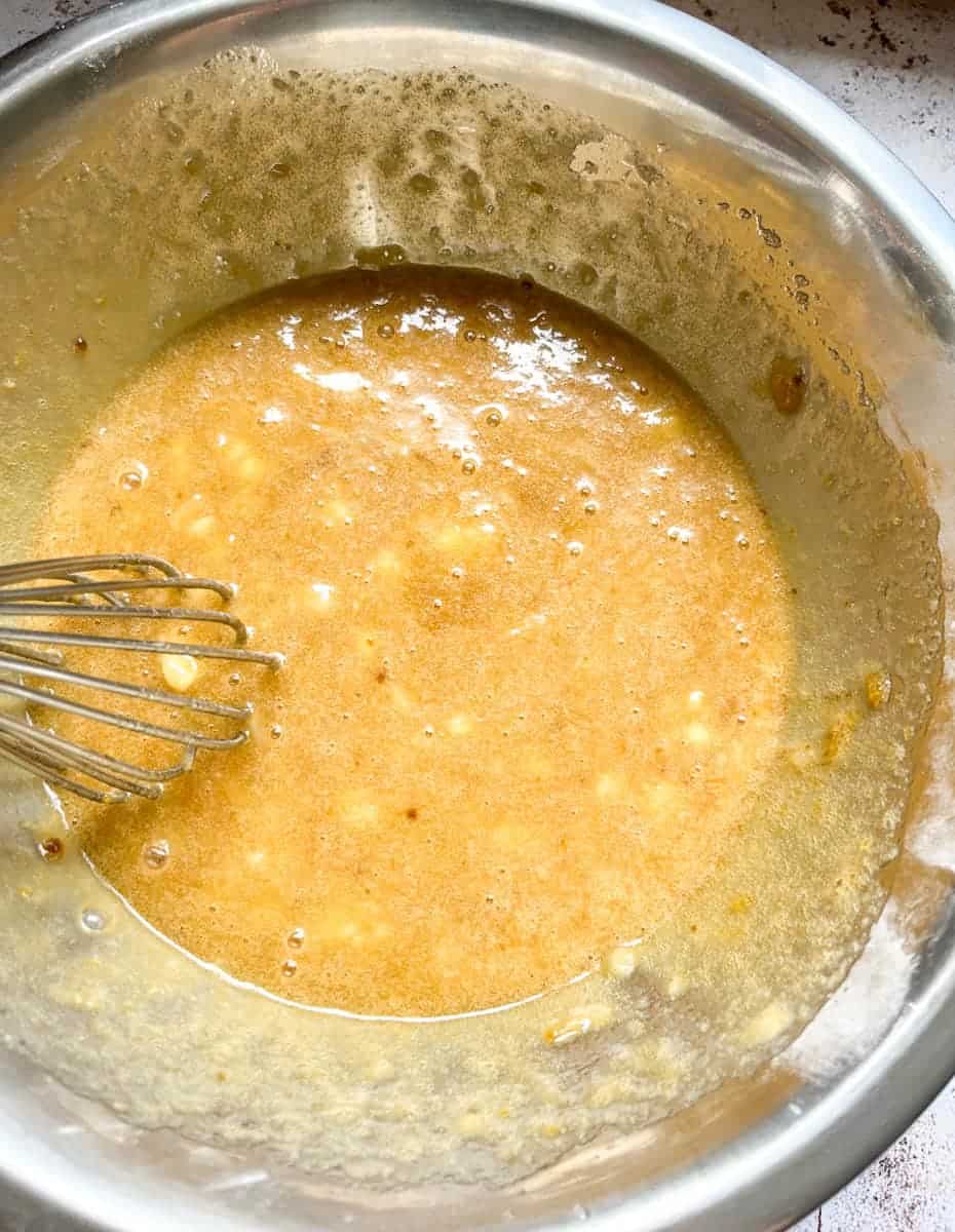 A large silver bowl of banana bread batter and a metal balloon whisk.