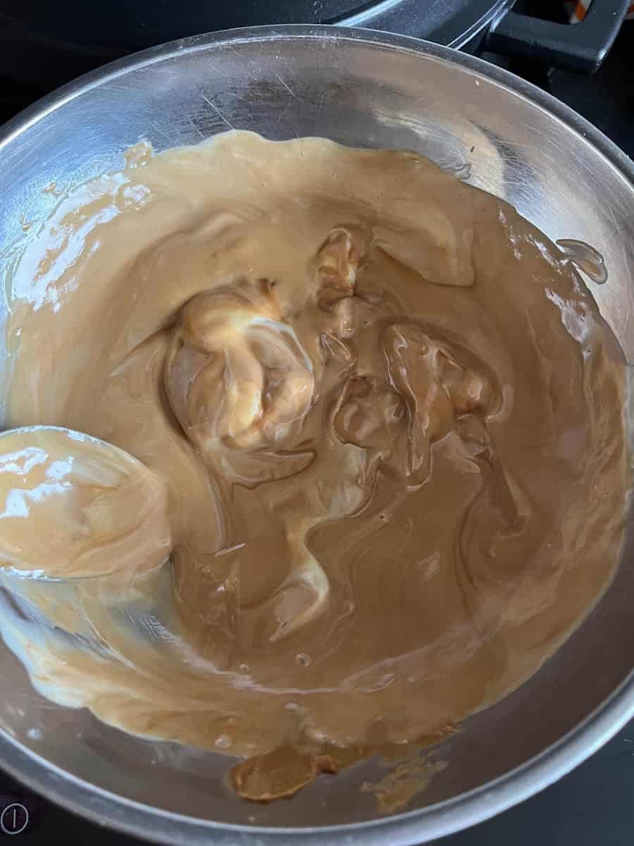 A silver bowl of melted biscoff spread and white chocolate.