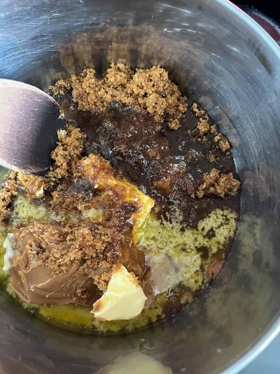 Brown sugar, Biscoff spread and butter melting in a silver saucepan.
