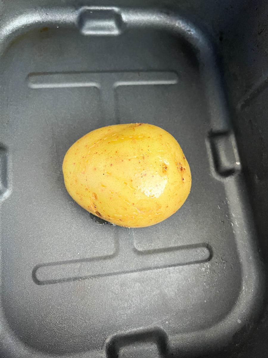 An uncooked baking potato inside an air fryer basket.