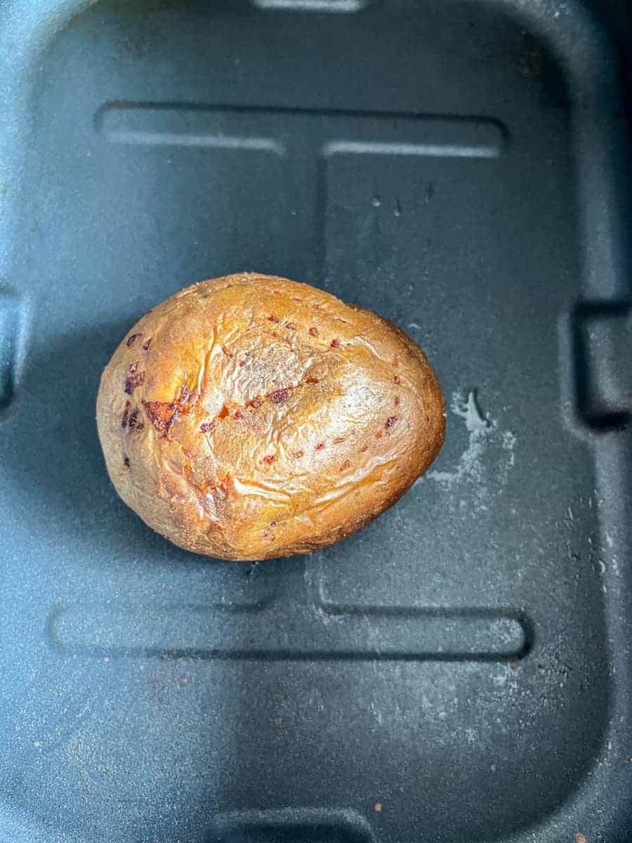 A baked potato inside an air fryer basket.