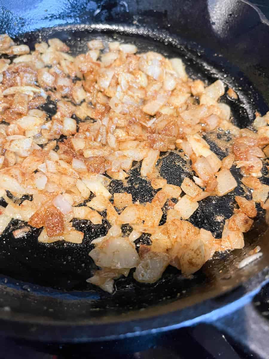 chopped onions and spices cooking in a black saucepan.