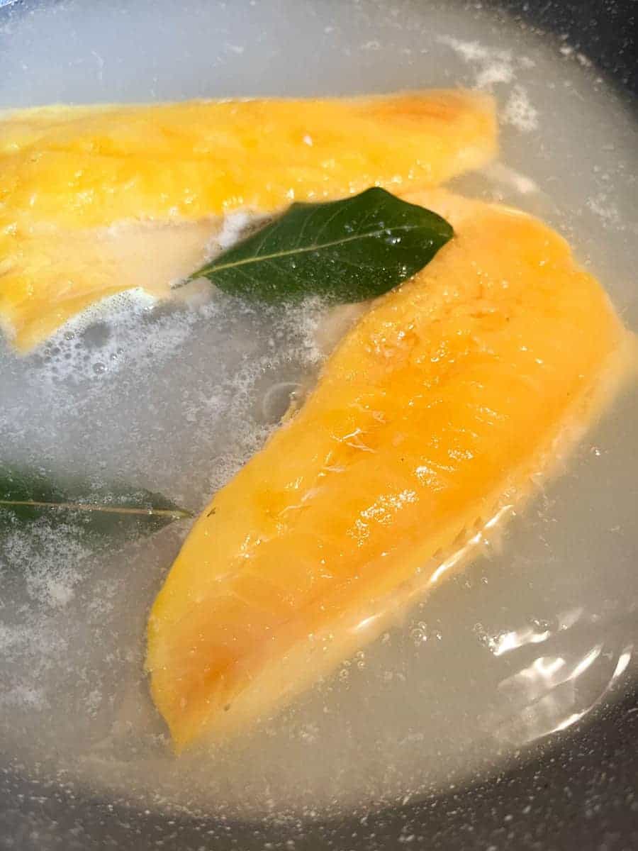 Two smoked haddock fillets and a bay leaf in a pan of simmering water.