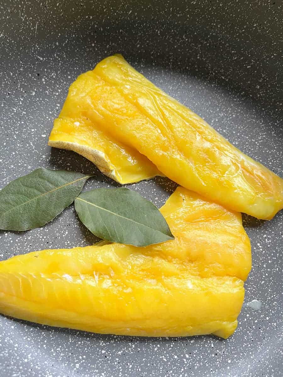 Two smoked haddock fillets and two bay leaves in a pan.