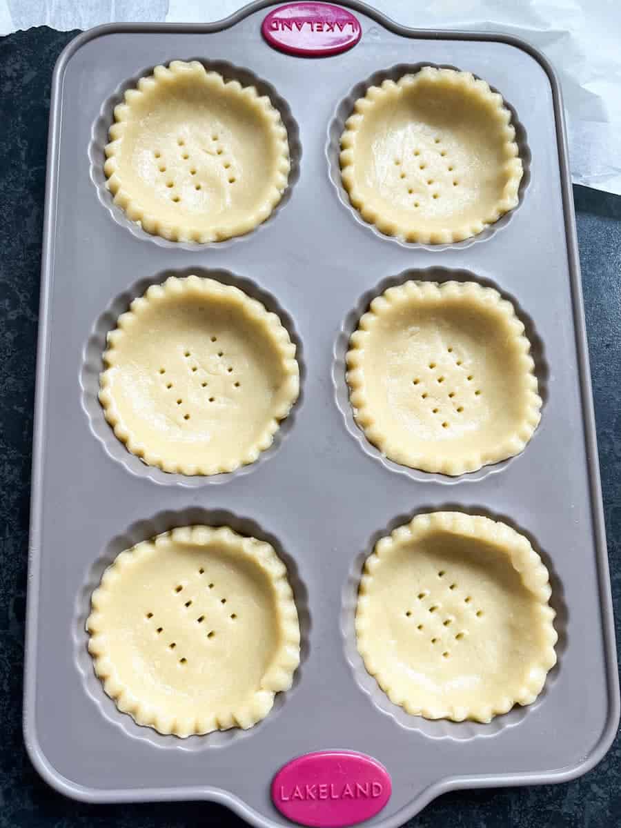 A grey six hole silicone tart tin with six unbaked pastry shells.