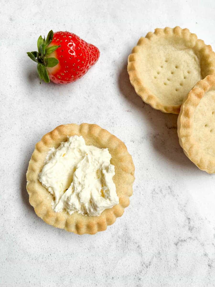 A strawberry and three small tart shells, one filled with whipped cream.