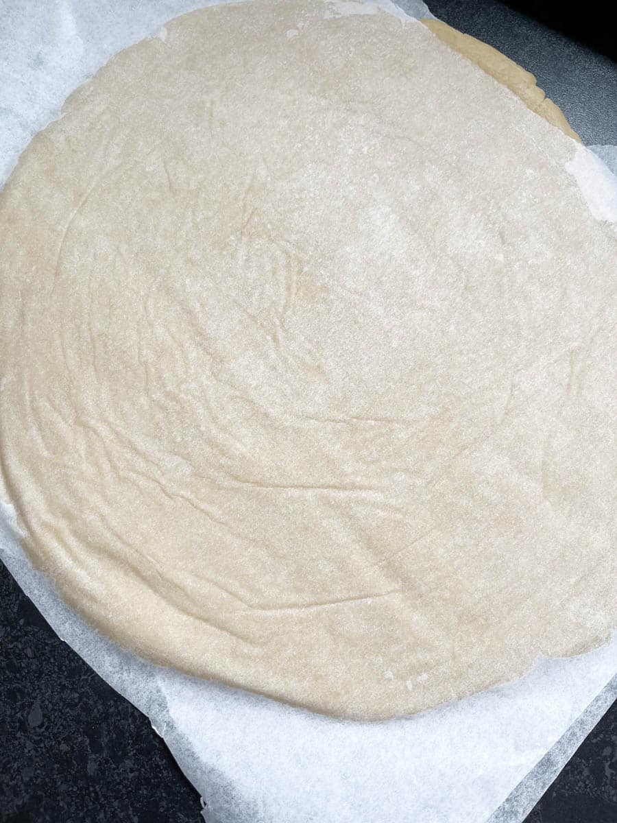 A rolled out piece of sweet pastry dough between two sheets of baking paper.