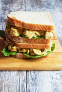 Two Coronation chicken sandwiches with lettuce stacked on top of each other on a wooden chopping board.