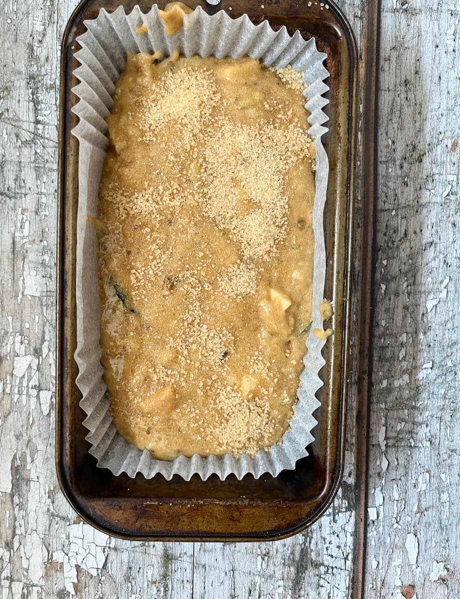 An unbaked zucchini walnut loaf cake sprinkled with demerara sugar in a loaf pan.