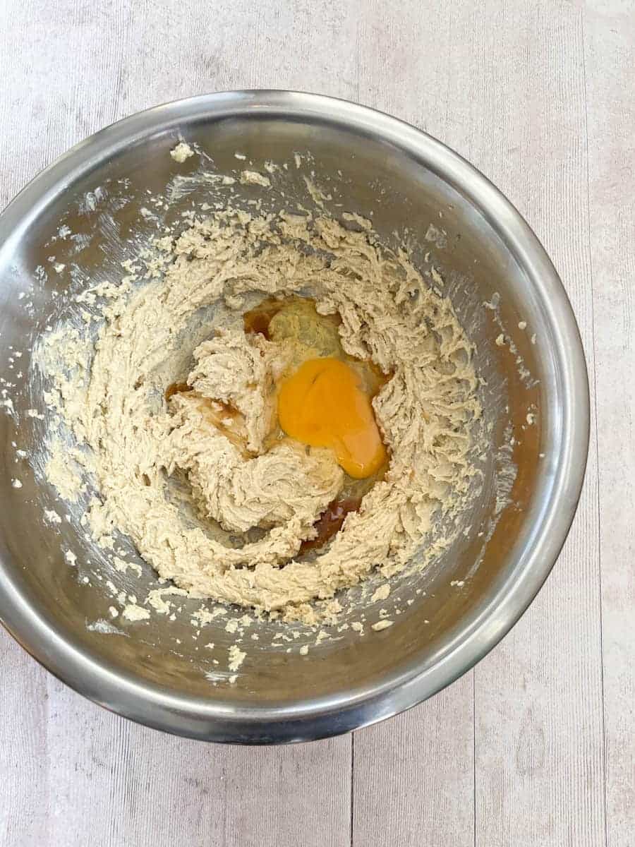 A large silver mixing bowl of creamed butter and sugar, egg and vanilla extract.