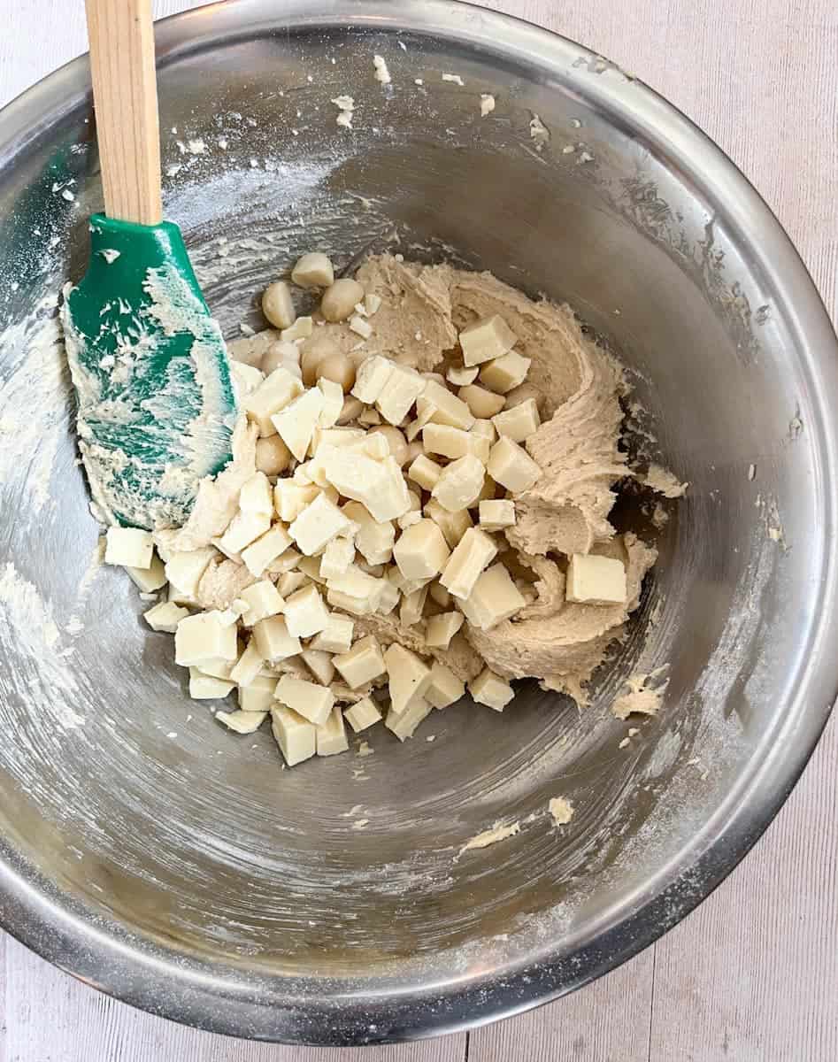 A silver bowl of white chocolate cookie dough and a green rubber spatula with a wooden handle.
