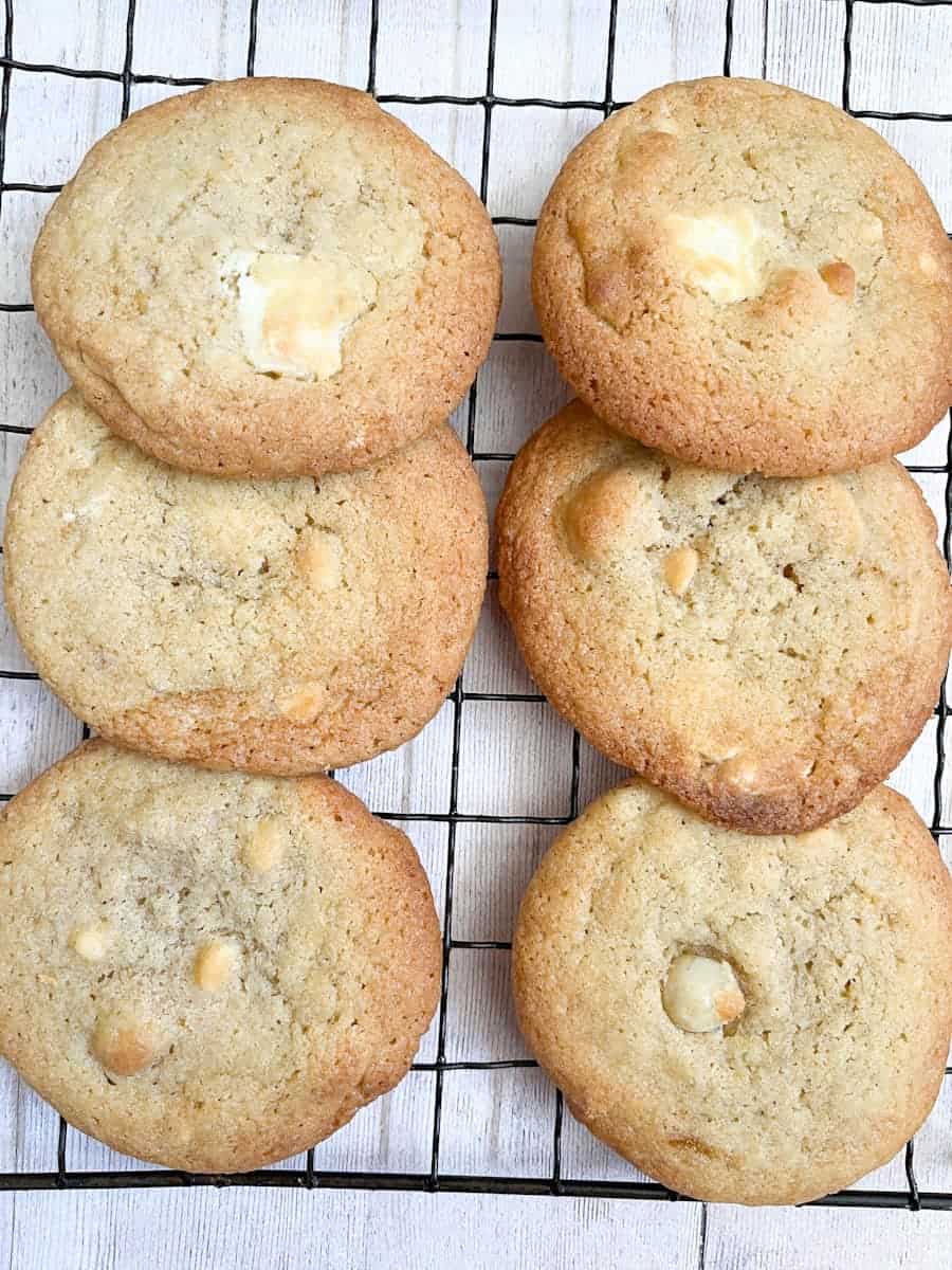 six white chocolate macadamia nut cookies on a black wire cooling rack.