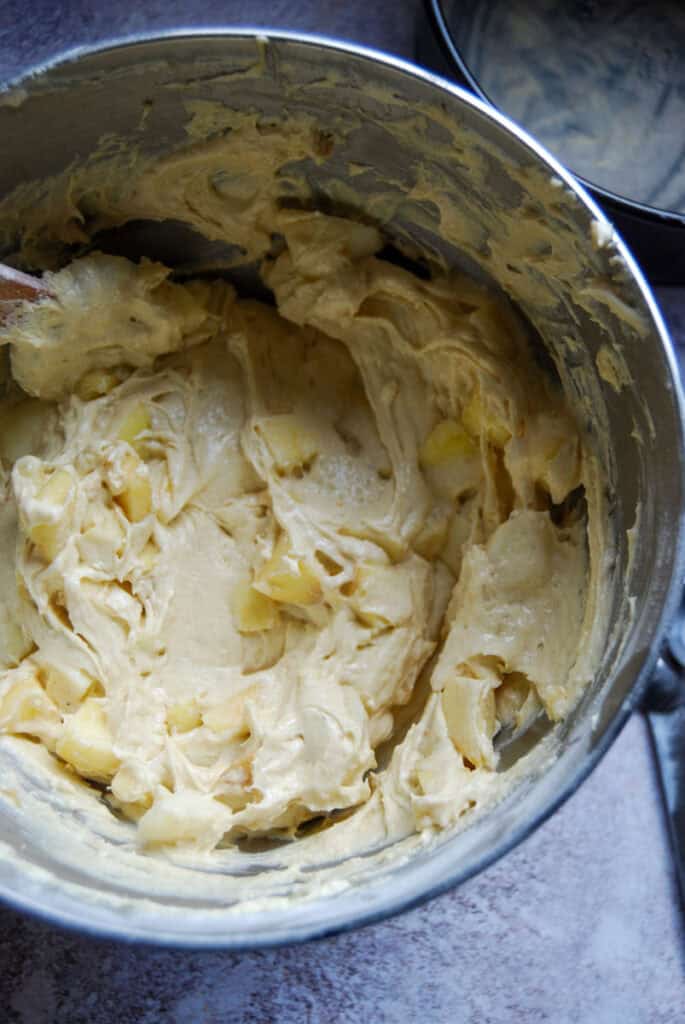Fresh diced apples being folded into a vanilla cake batter.