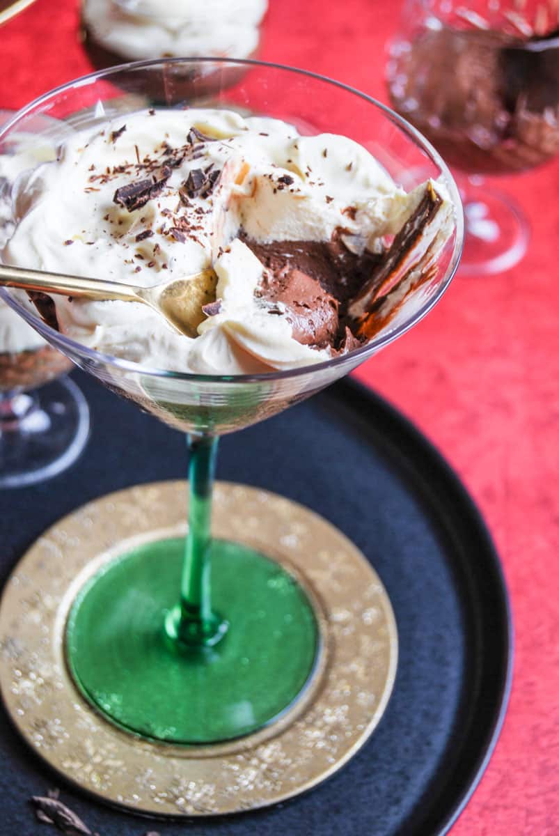 A green martini glass filled with chocolate mousse topped with whipped cream and grated chocolate with a gold spoon.