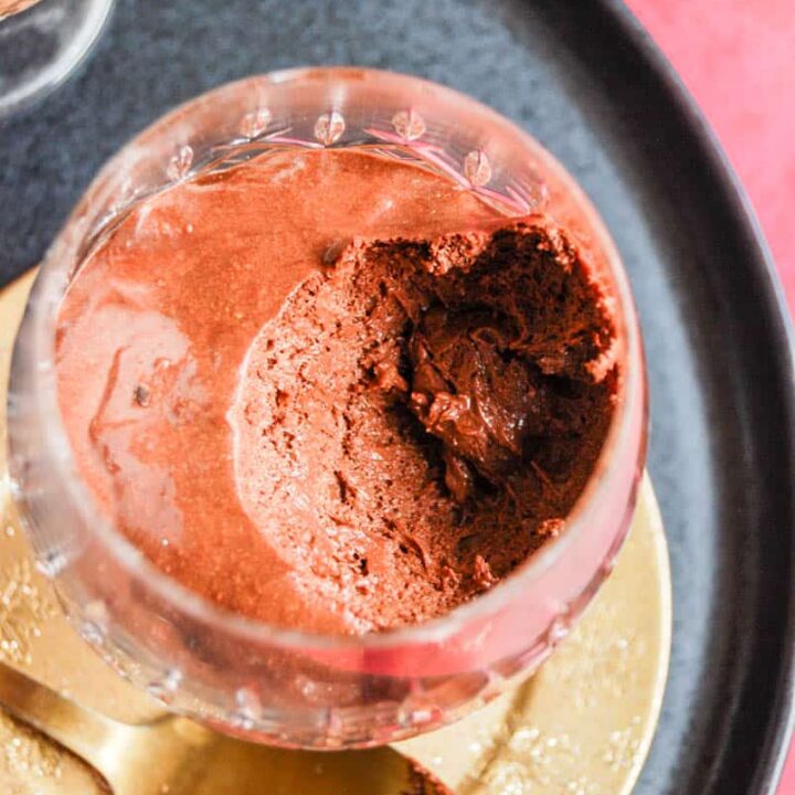 A crystal glass of chocolate mousse on a gold coaster and black plate.