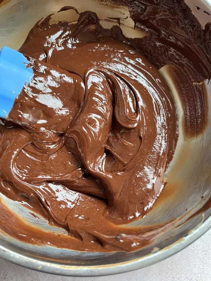 A silver bowl of melted chocolate and a blue spatula.