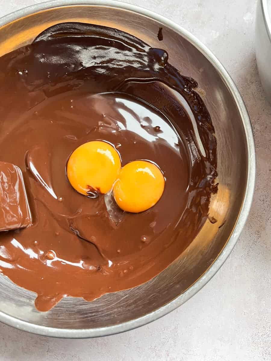 A silver bowl of melted dark chocolate with egg yolks.