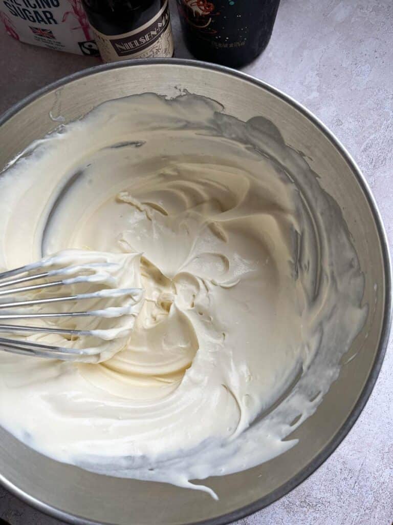 A silver bowl of whipped cream and a silver whisk.