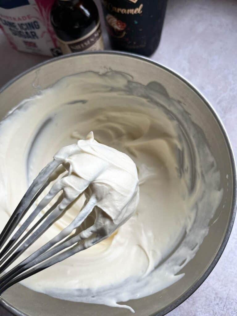 A silver bowl of softly whipped cream and a silver whisk.