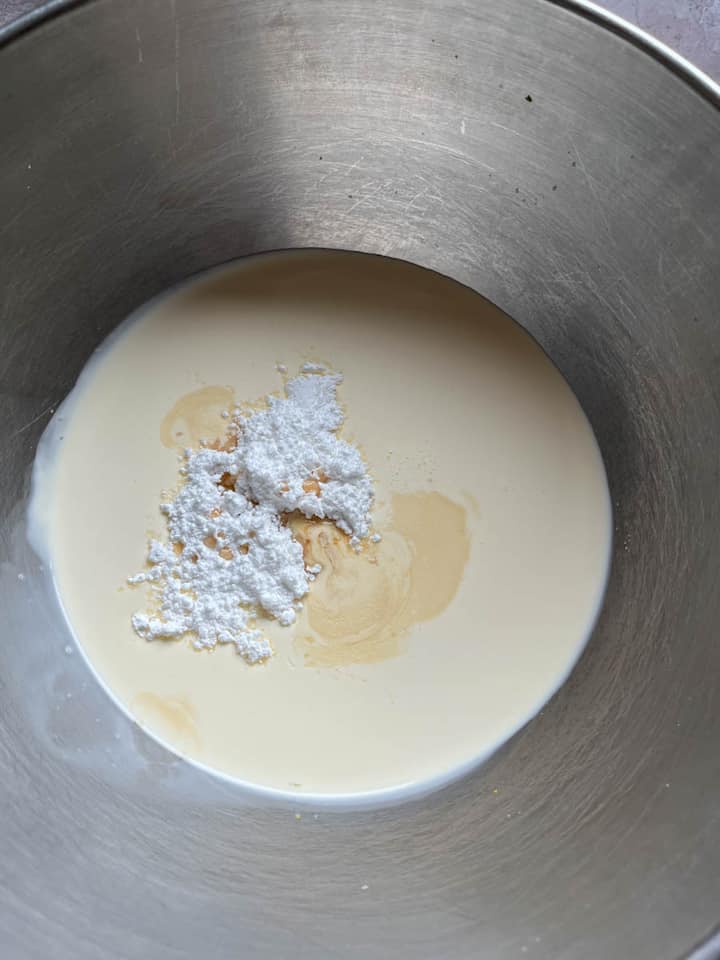 A silver bowl of cream with icing sugar and vanilla extract.