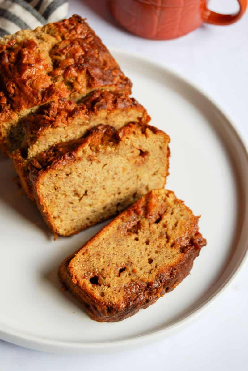 A partially sliced banana cake with fudge pieces on a white plate.