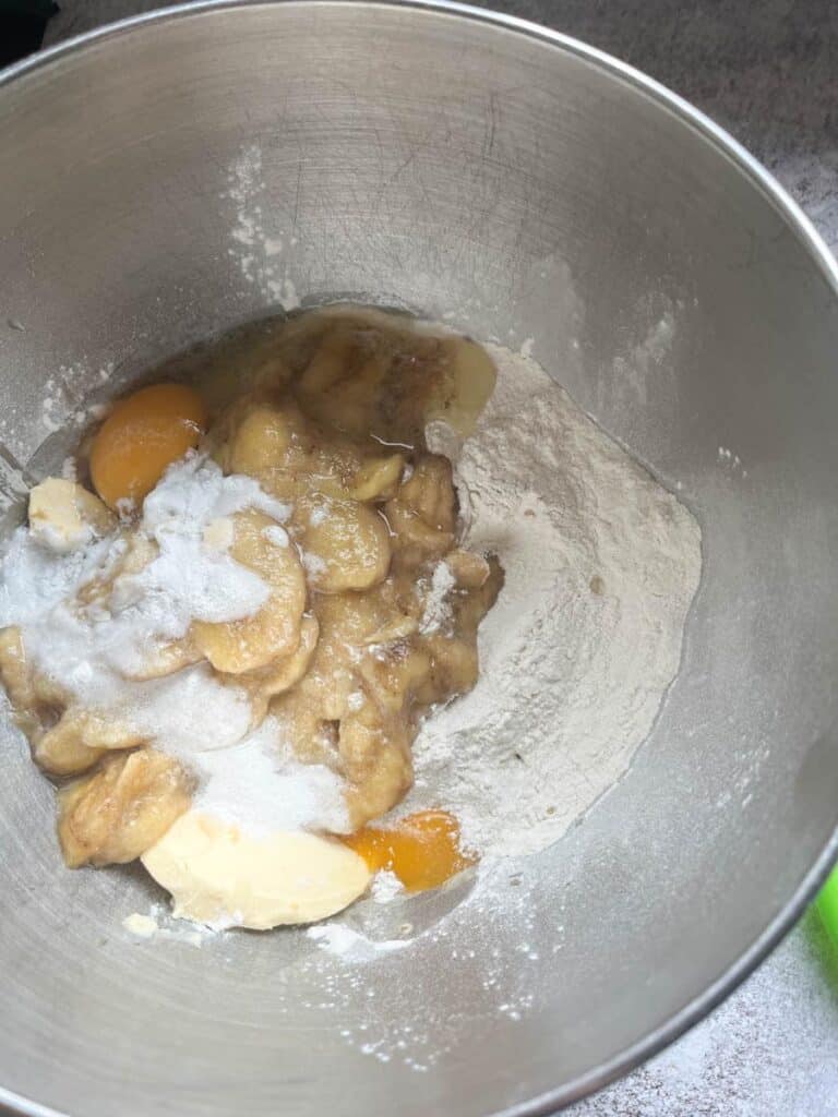 A silver bowl of flour, mashed bananas, butter, eggs and sugar.