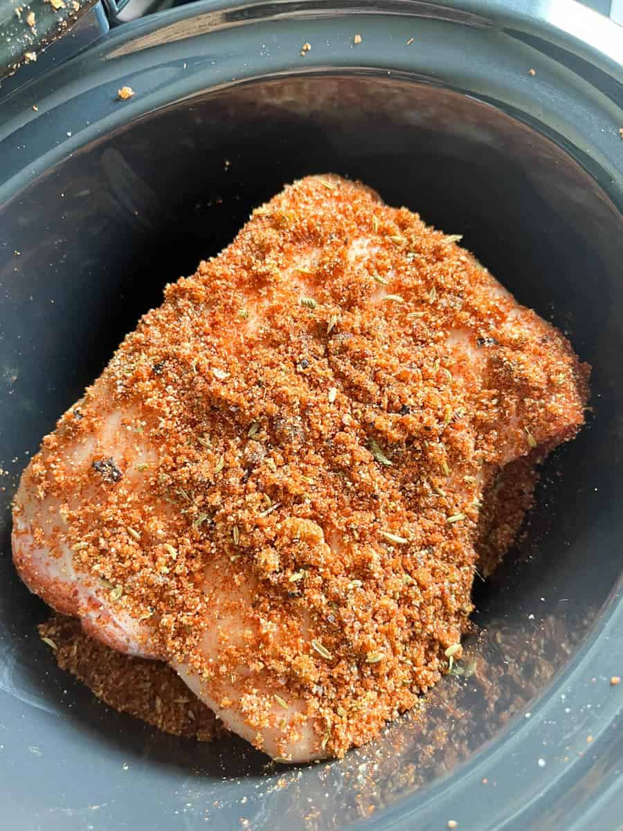 A pork shoulder joint covered in a spicy rub inside a slow cooker.