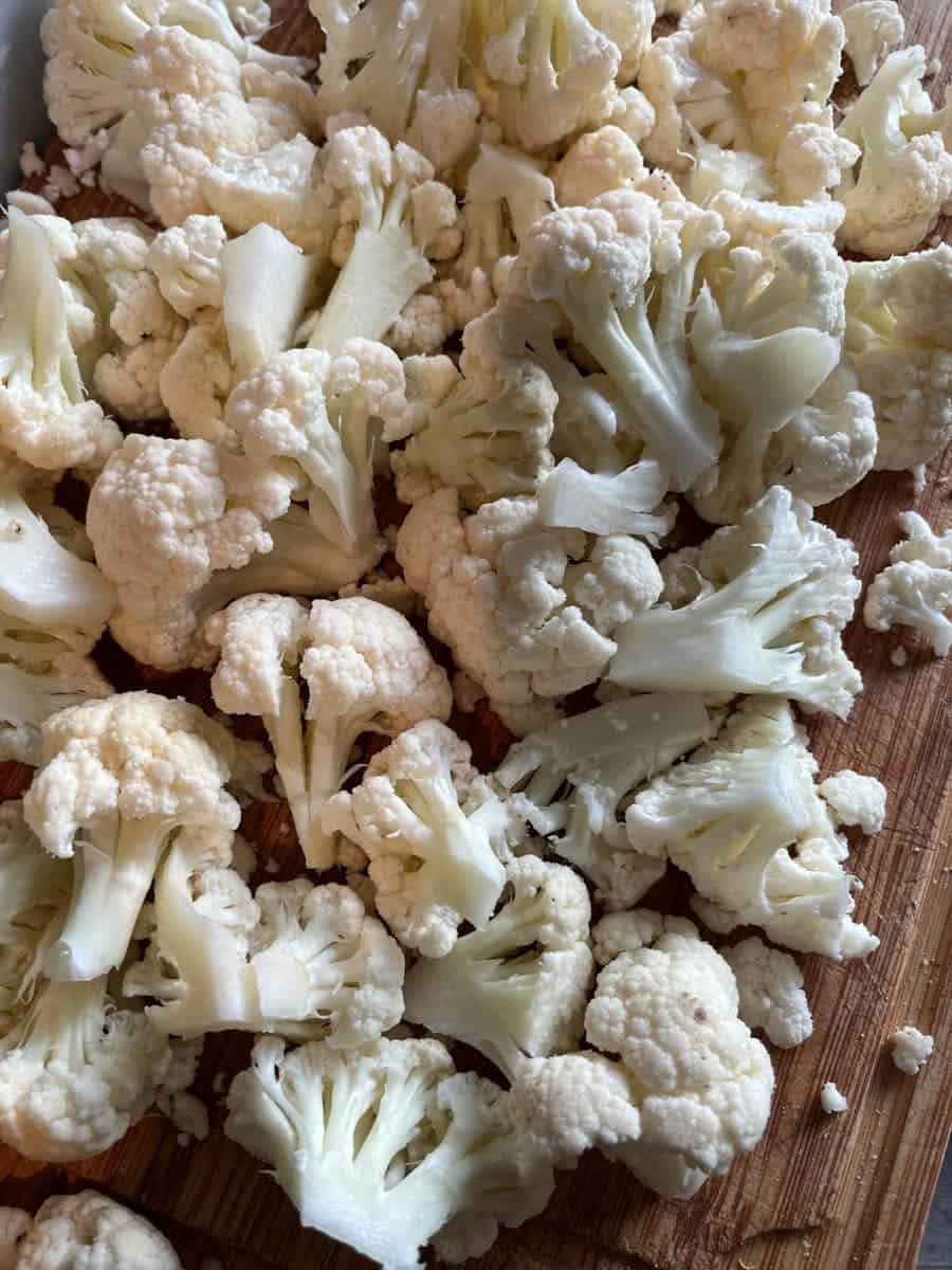 Chopped cauliflower florets on a wooden chopping board.