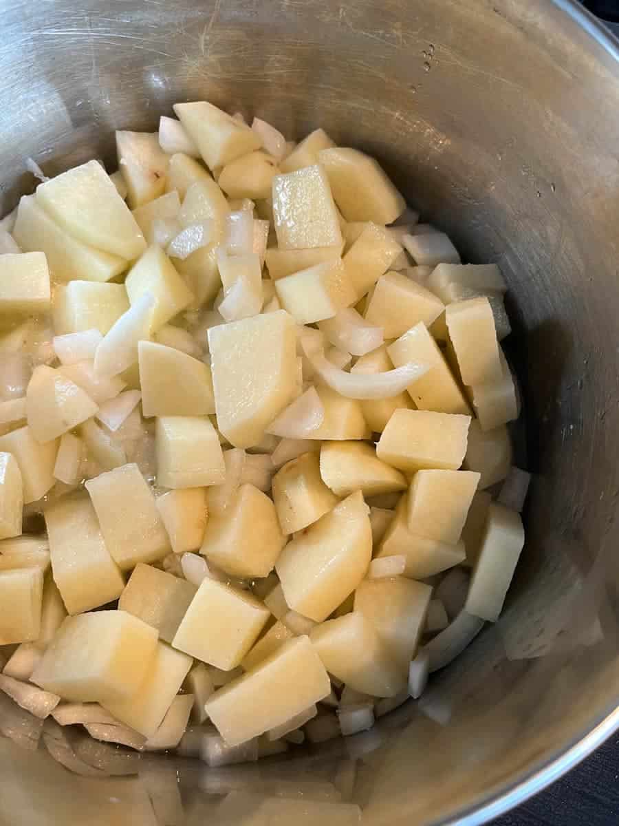 Diced onion and potato in a silver saucepan.
