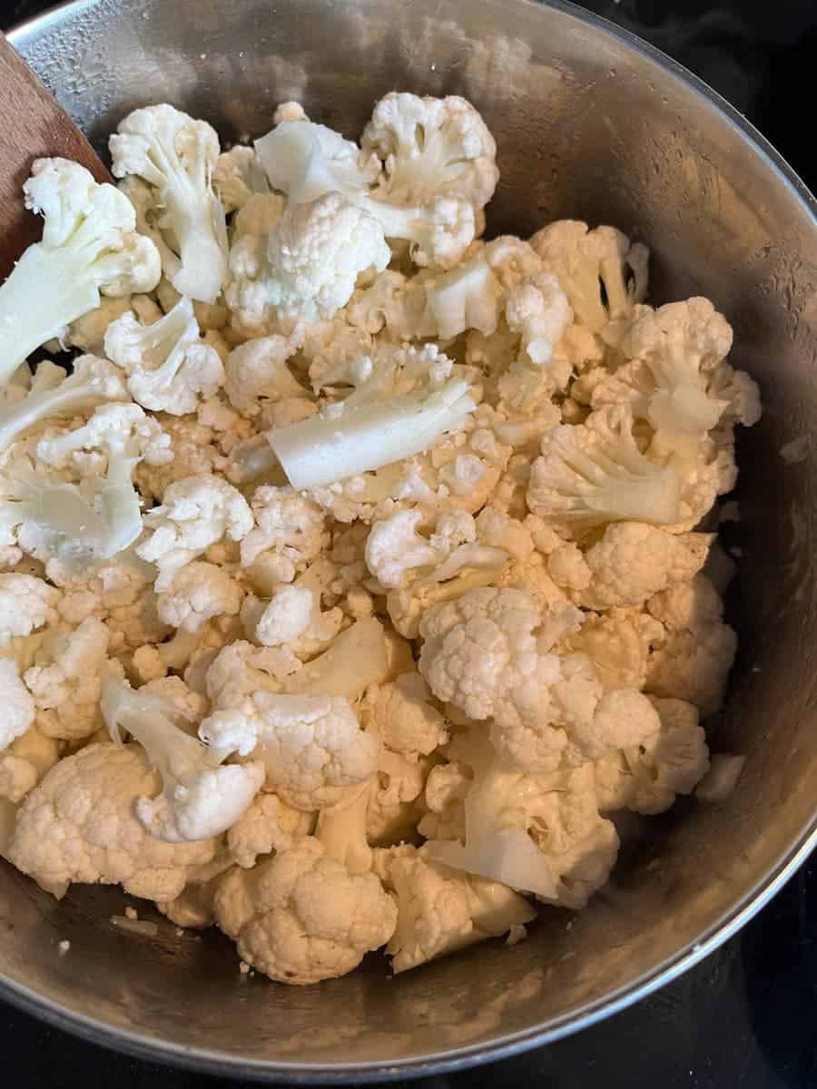 Chopped cauliflower florets in a silver pan.