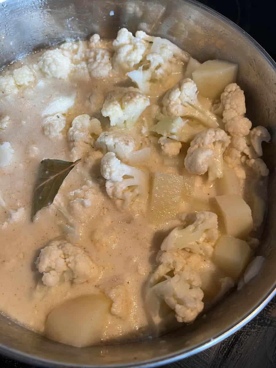Chopped cauliflower, milk, stock and a bay leaf in a silver pan for soup.
