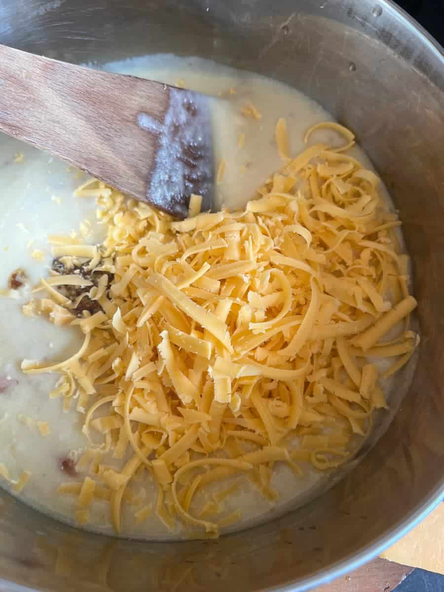 Grated cheese and mustard being stirred into soup with a wooden spoon,