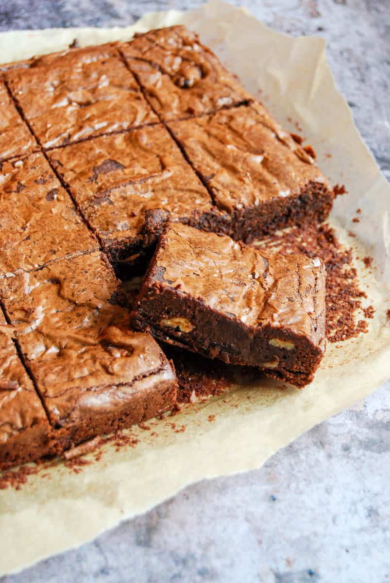 A batch of chocolate brownies with chopped pecan nuts on a piece of baking parchment.