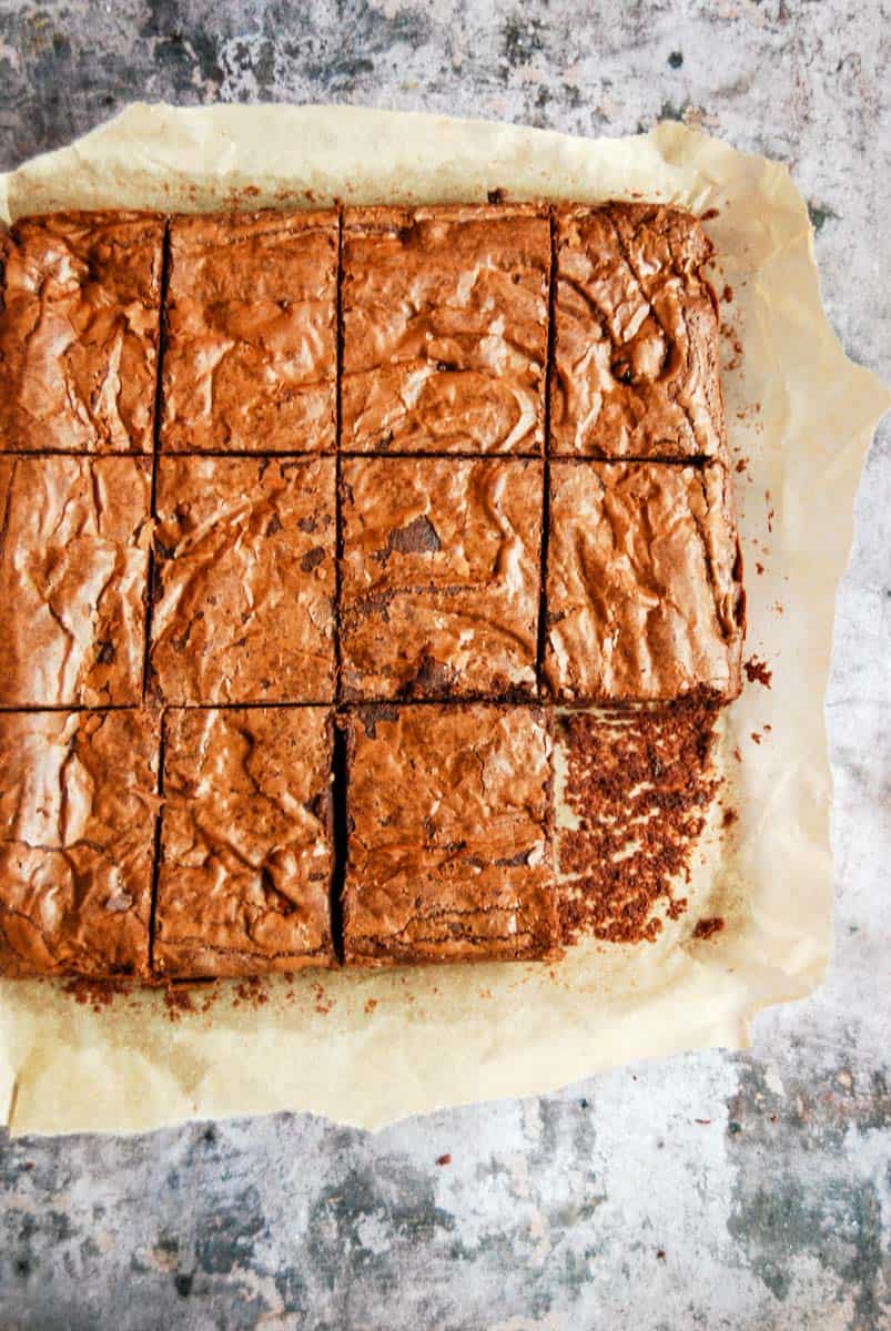 A chocolate brownie cut into 12 squares with one piece missing.