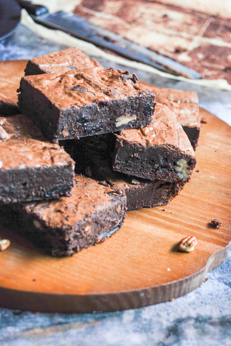 A batch of chocolate brownies with dried cherries and pecan nuts on a wooden board.