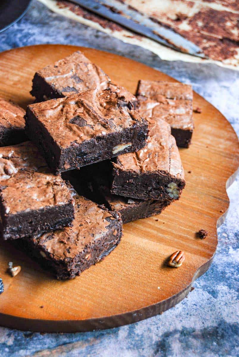 A batch of chocolate brownies with dried cherries and chopped pecan nuts on a wooden serving board.